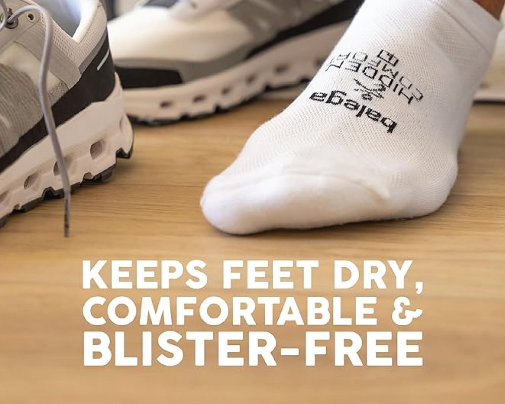 A foot wearing a white athletic sock with branding, next to a pair of modern running shoes, on a wooden surface. Text on the image states: "KEEPS FEET DRY, COMFORTABLE & BLISTER-FREE."