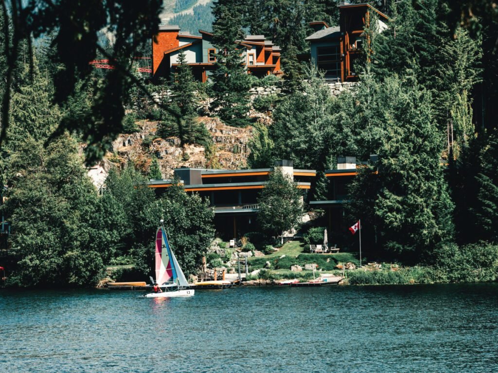 A lakeside resort in Canada with a sailboat on the water in the foreground and a Canadian flag on the shore.