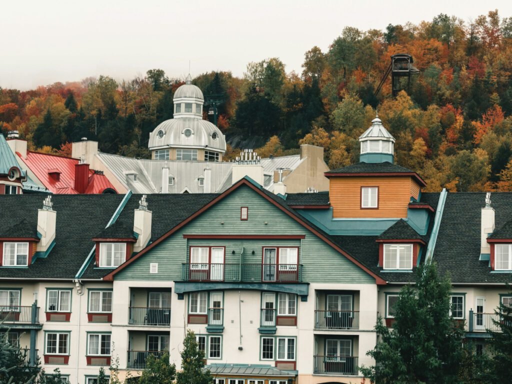 The colorful buildings of a resort with a ski lift visible in the background against a hill covered with autumn trees.