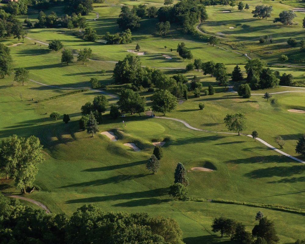 An aerial view of a sprawling, scenic golf course with lush green fairways, scattered trees, and winding cart paths, representing a beautiful provincial park golf course.