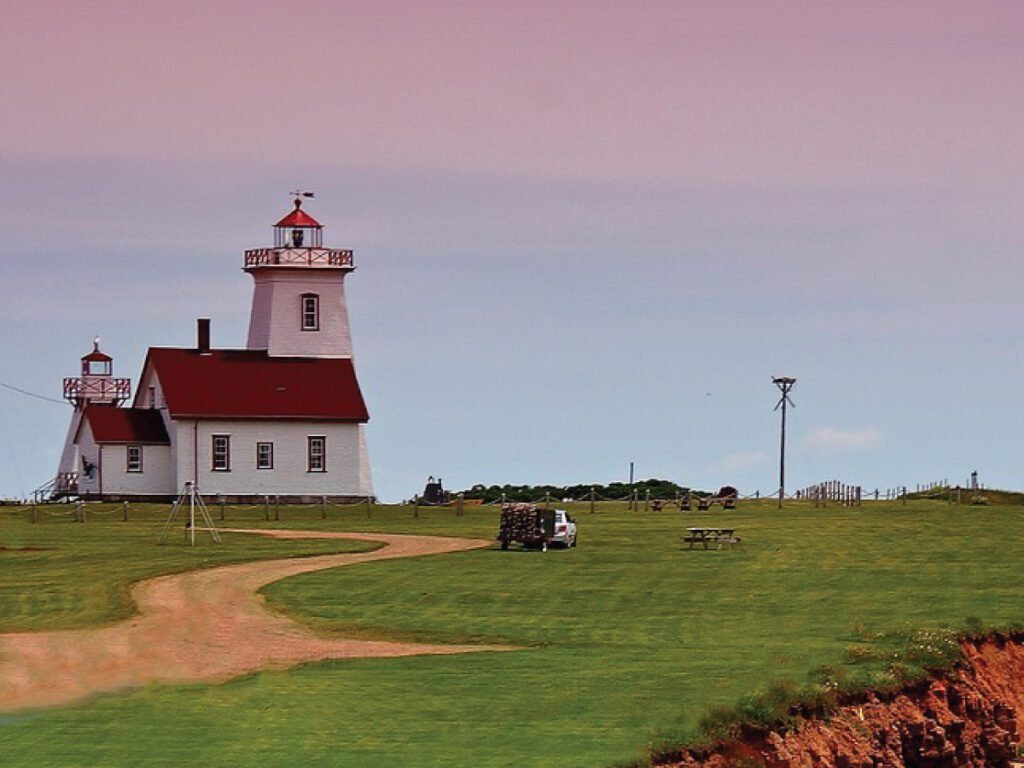 The East Point Lighthouse in Prince Edward Island, Canada, with a red roof and a white exterior, surrounded by green grass and a gravel road.