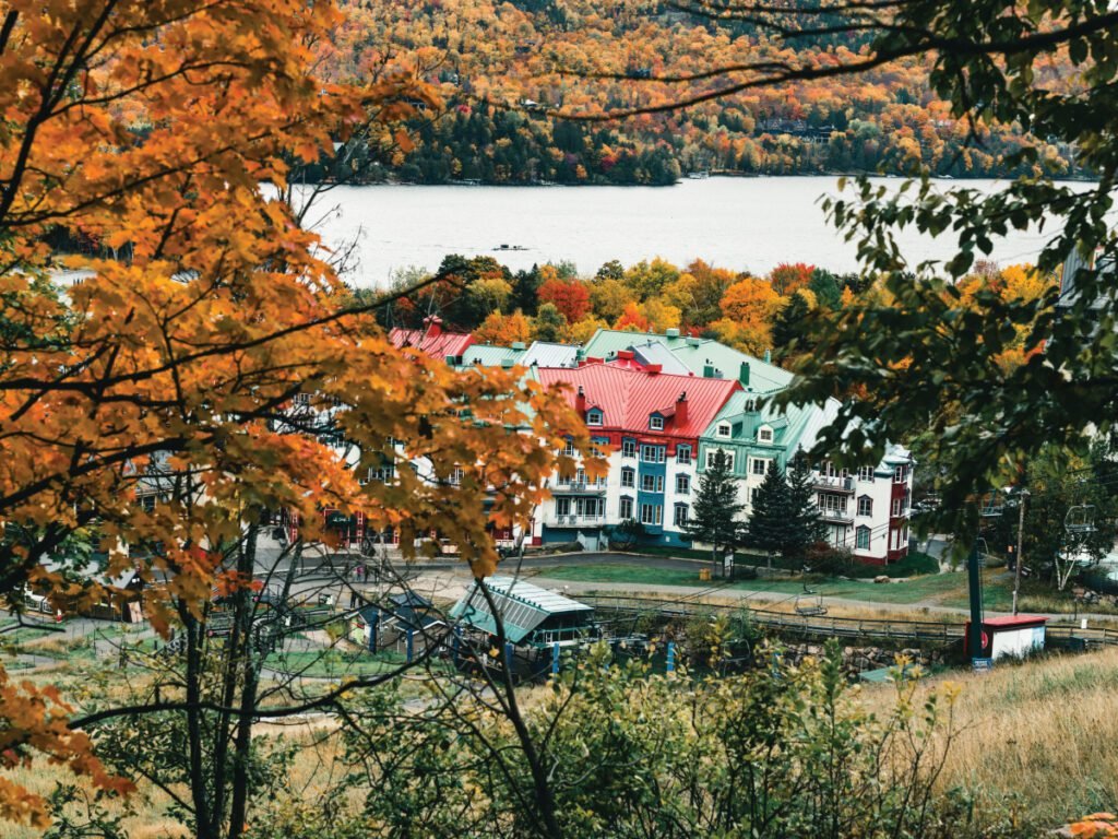 A scenic view of colorful buildings with red and green roofs on the shore of a lake, surrounded by autumn trees.