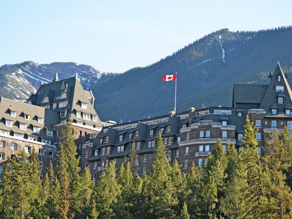  The Fairmont Banff Springs hotel in Banff National Park, Canada, with a Canadian flag flying on top and mountains in the background.